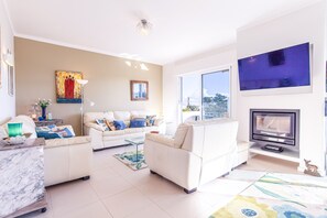 A modern living room with a white sofa set, a flat-screen TV, and a fireplace.