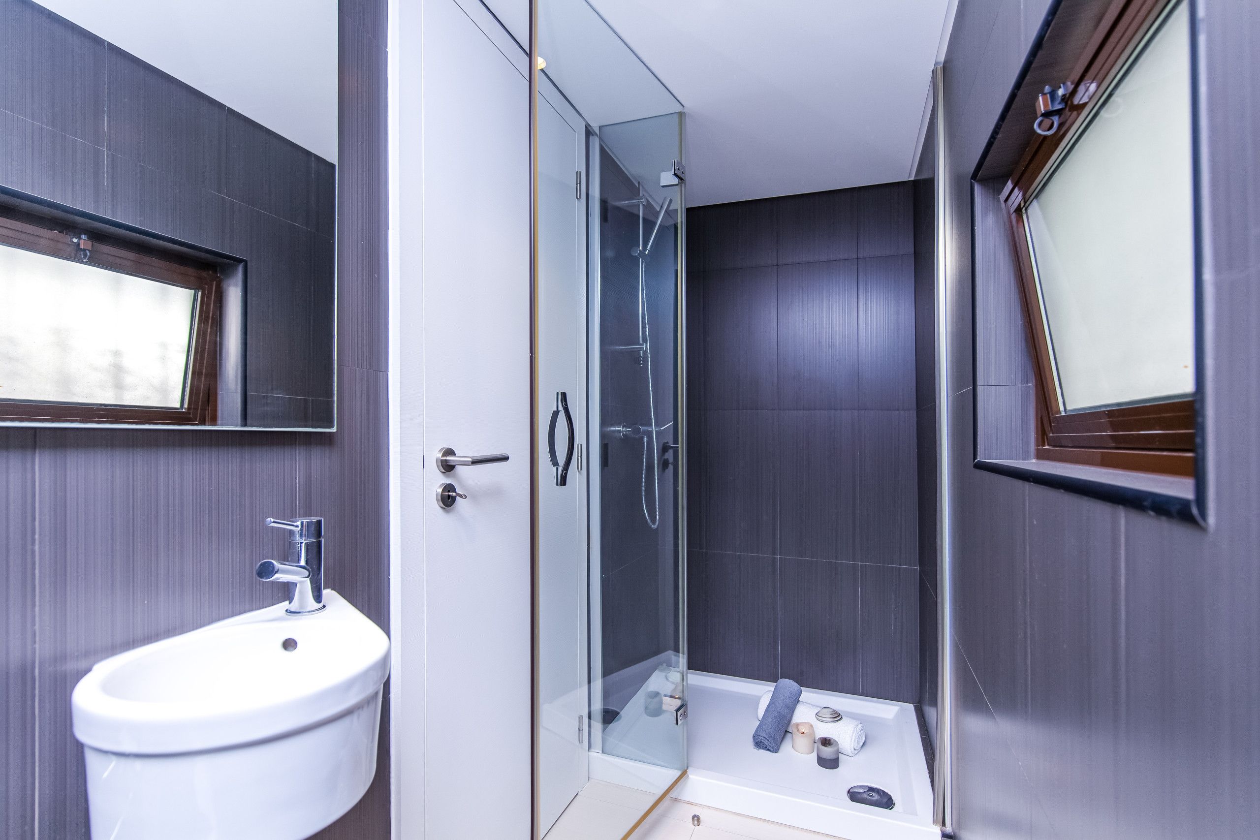 Un baño moderno con ducha de vidrio, lavamanos blanco y un espejo grande.