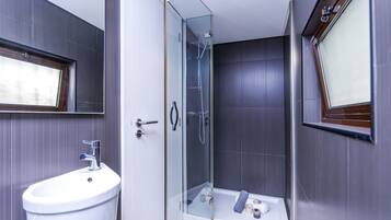 Un baño moderno con ducha de vidrio, lavamanos blanco y un espejo grande.