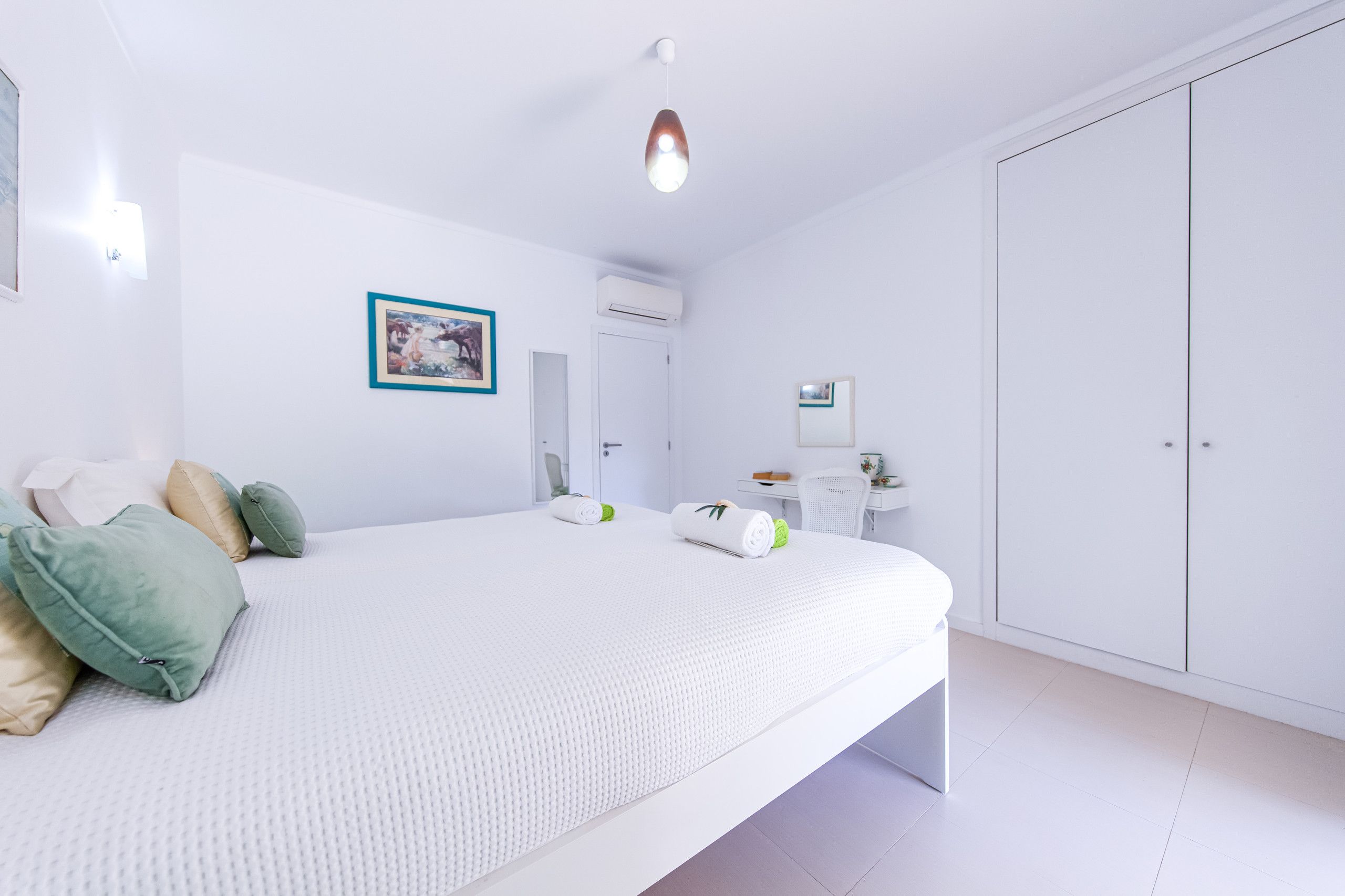 A modern bedroom with a large bed, a desk, and a wardrobe.