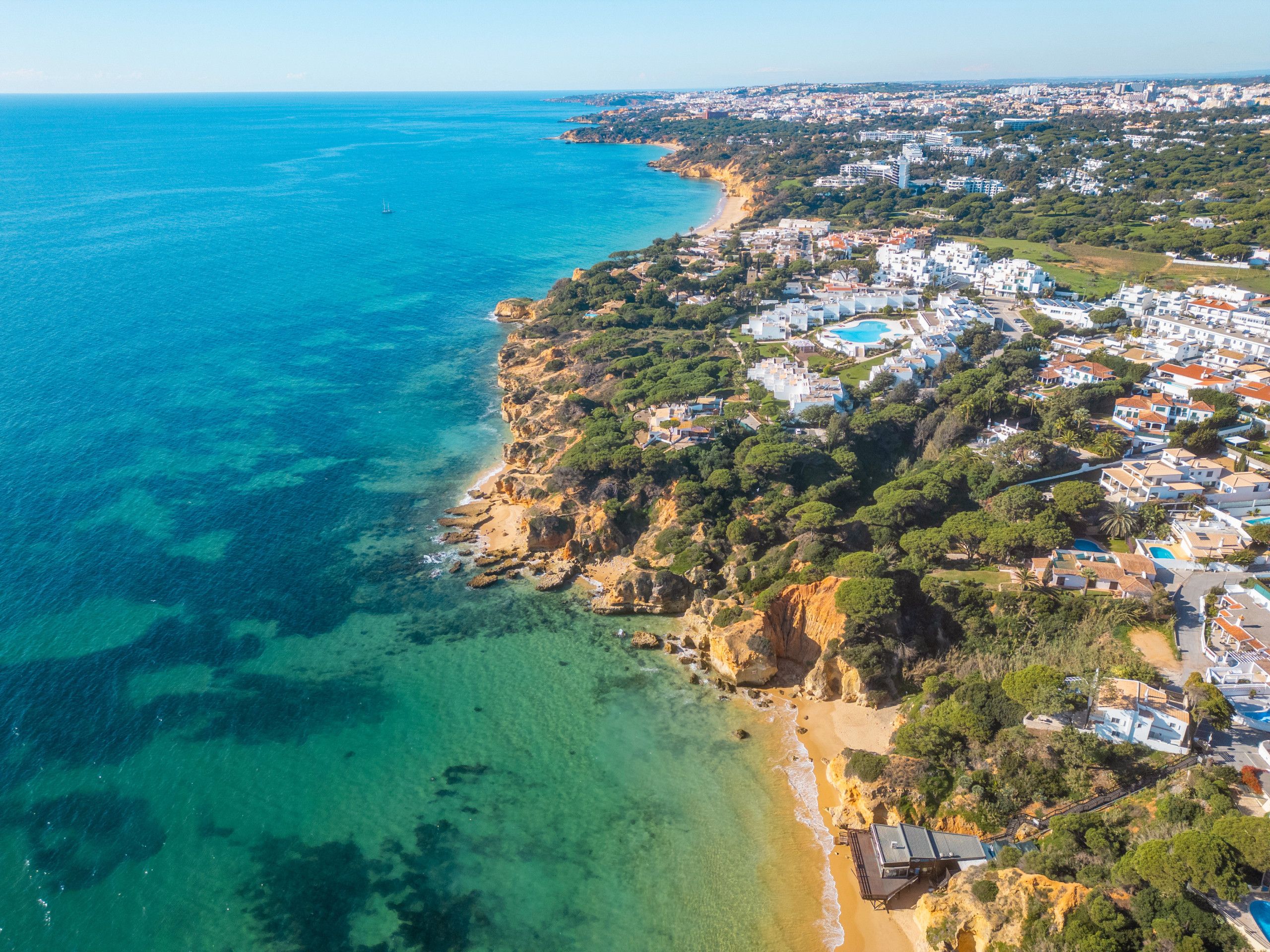 An aerial view of a coastal town with a beach, clear waters, and residential buildings.