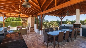 Un patio al aire libre con techo de madera, una mesa con cubierta de vidrio, sillas de mimbre y una chimenea de piedra.