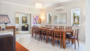 Un comedor con una mesa y sillas de madera, una araña y un cuadro grande en la pared.