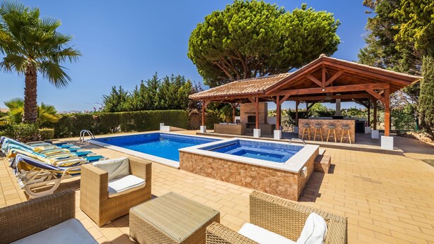 Un área de piscina con sillones de descanso y una zona de estar techada.
