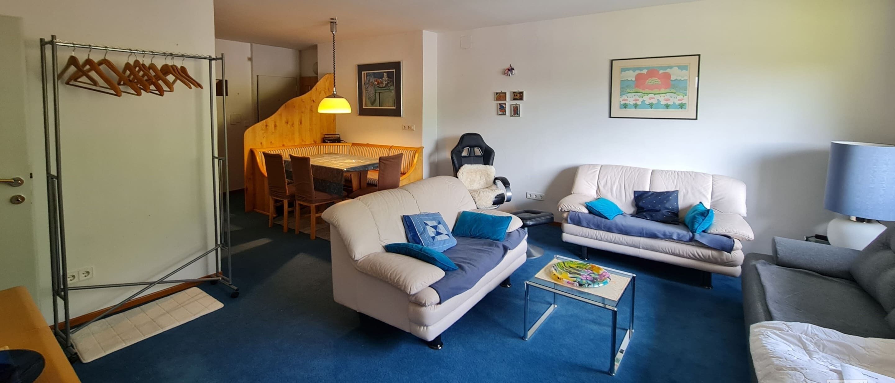 A living room with two sofas, a coffee table, and a lamp. There is a dining area with a table and chairs in the background.