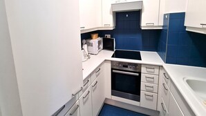 Una cocina compacta con armarios blancos, microondas, horno y lavaplatos.