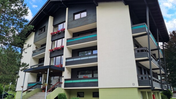 Un edificio de varios pisos con balcones, una escalera y un pequeño jardín.