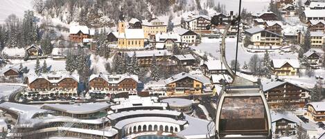A snow-covered village with traditional wooden buildings, a ski lift, and a pool area.