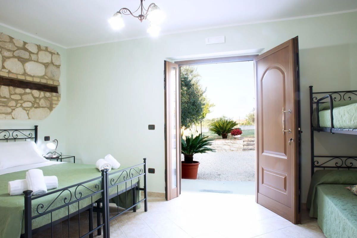 A bedroom with a bed, a nightstand, a potted plant, and a door leading to an outdoor area.