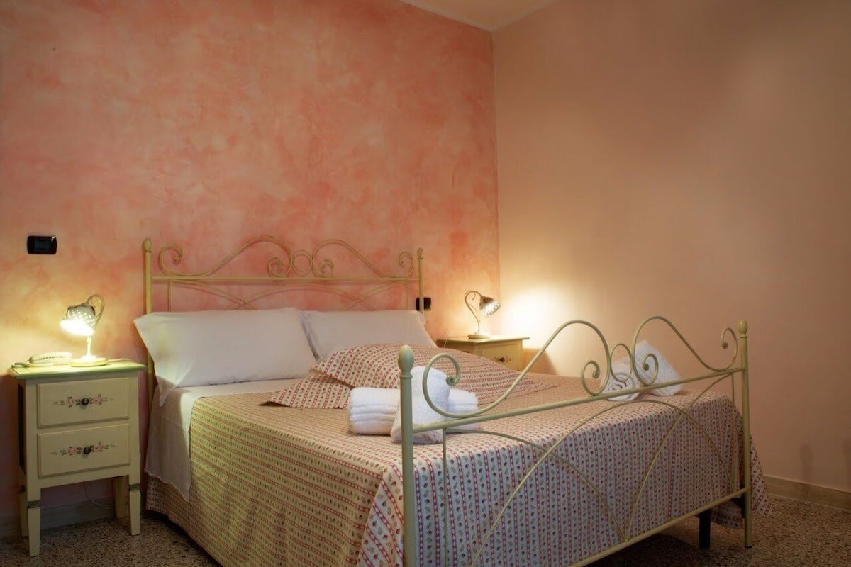 A neatly made bed with a metal frame, a bedside table with a lamp, and a wall with a textured finish.