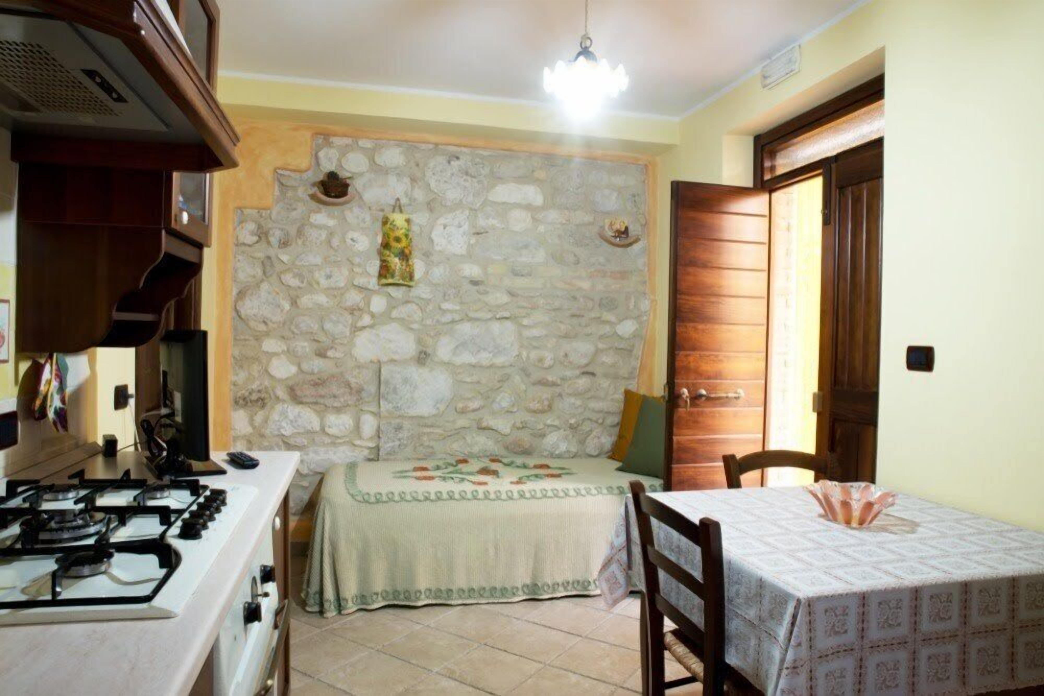 Une cuisine équipée d’une cuisinière à gaz, avec un mur en pierre, une porte en bois et une table à manger recouverte d’une nappe.