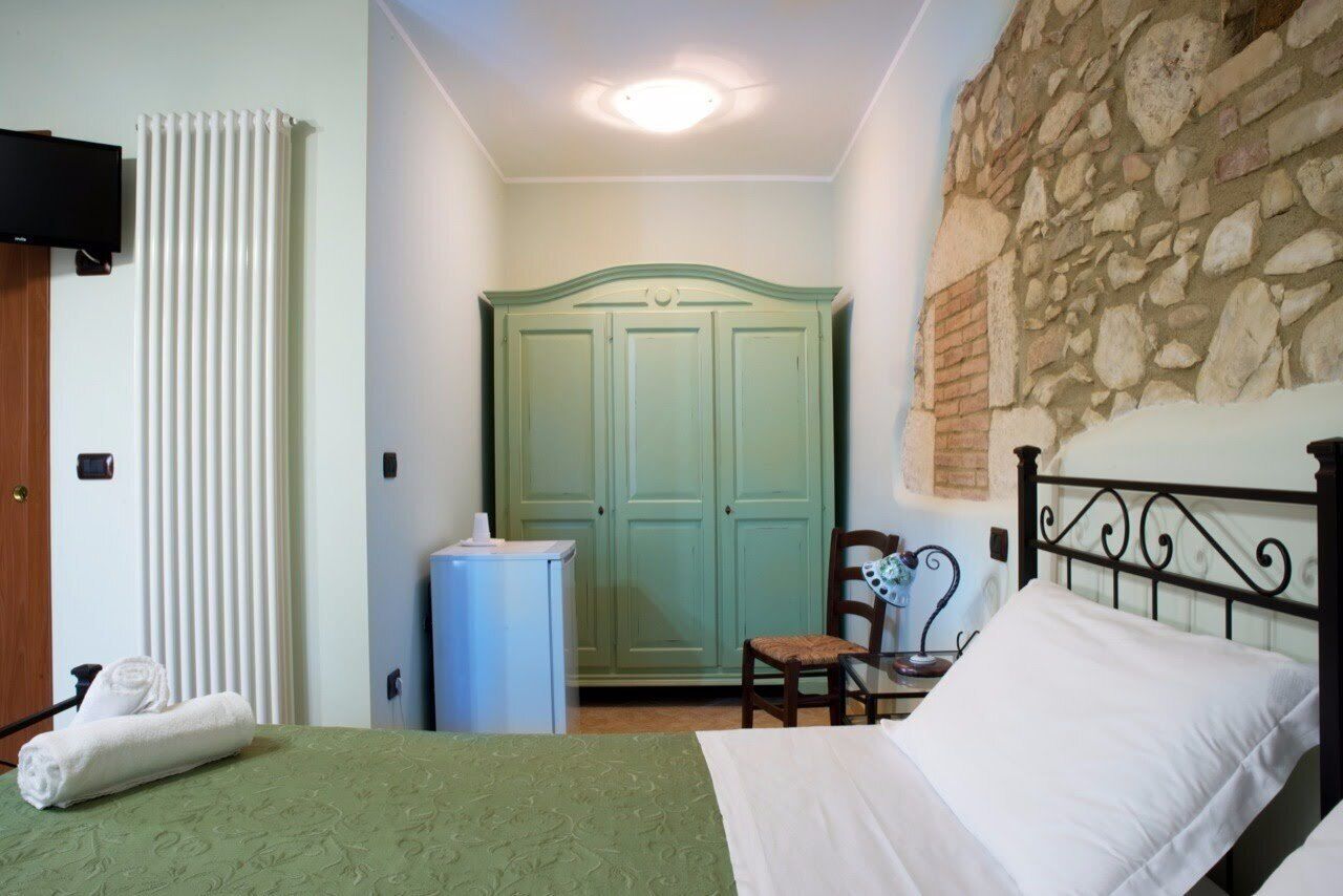 Ein Schlafzimmer mit einem Bett, einem Sessel, einem Schreibtisch, einem Heizkörper, einem Kleiderschrank und einer Steinwand.