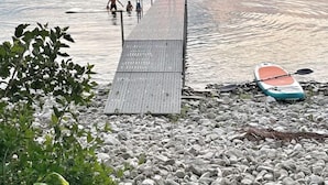 Un muelle de madera que se adentra en aguas tranquilas, rodeado de guijarros y follaje.