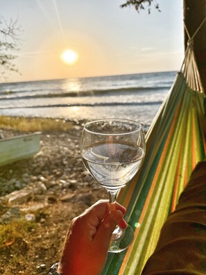 A person holding a glass of water with a view of the ocean and a hammock.