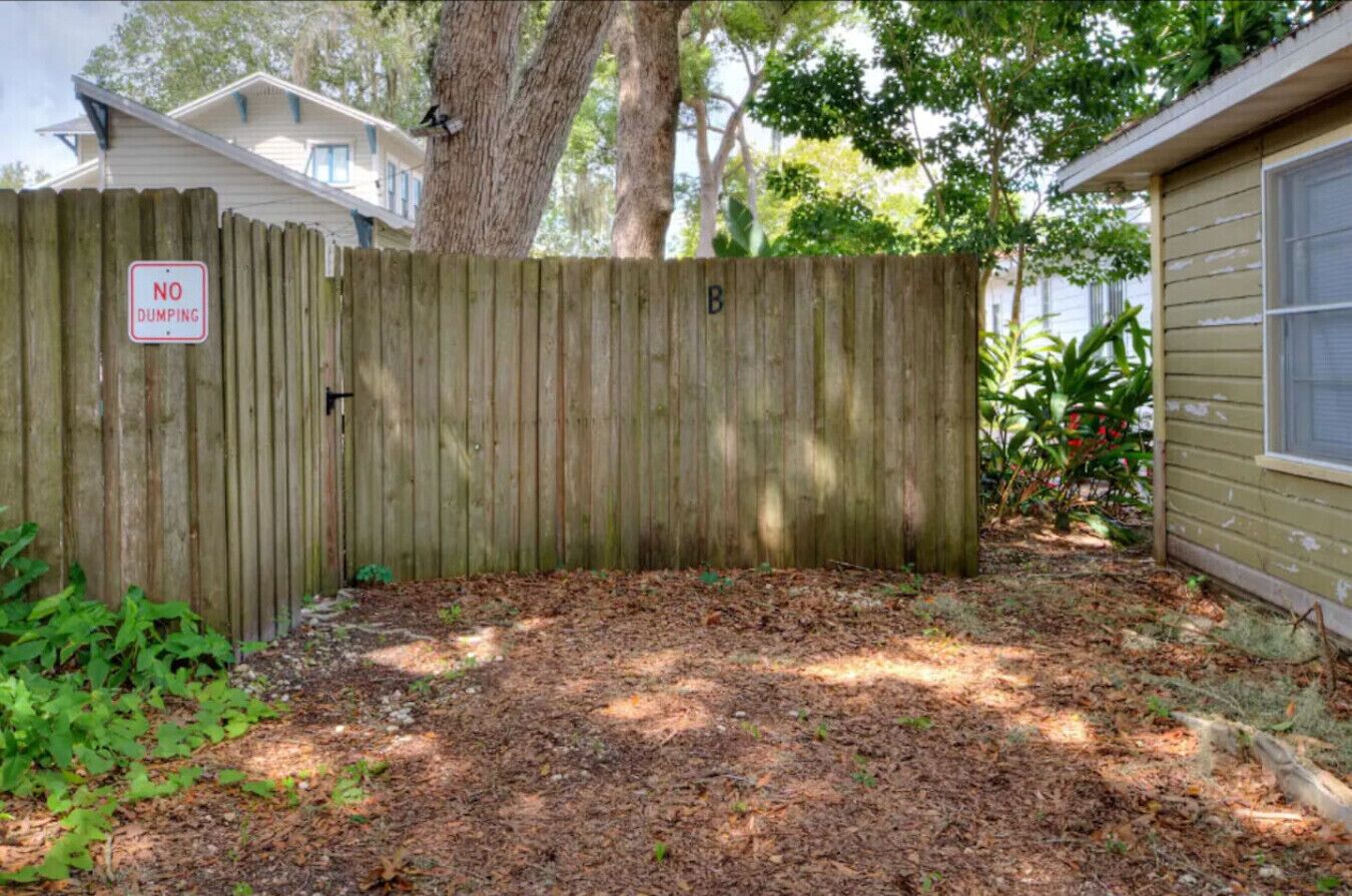 A wooden fence with a 'NO DUMPING' sign, a yard with mulch, and a house with a window.