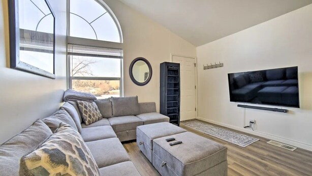 A modern living room with a sectional sofa, ottoman, and a flat-screen TV mounted on the wall. - Cozy 2-bedroom house in Reno near UNR - Sleeps 7 (Reno)