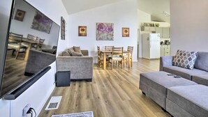 A modern living room with a grey sofa, a dining area with wooden furniture, and a kitchen in the background. - Cozy 2-bedroom house in Reno near UNR - Sleeps 7 (Reno)