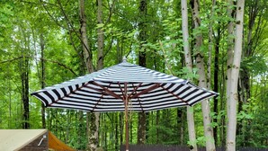 Une terrasse en bois avec une table ronde et des chaises, un parasol à rayures et une clôture en bois, le tout situé dans un espace boisé.