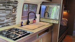Une petite cuisine équipée avec une cuisinière à gaz, un évier et une petite fenêtre.
