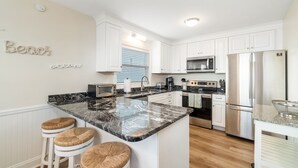 A modern kitchen with white cabinets, a granite island, and stainless steel appliances. - Charming 5-bedroom oceanfront duplex with wonderful views (Emerald Isle)