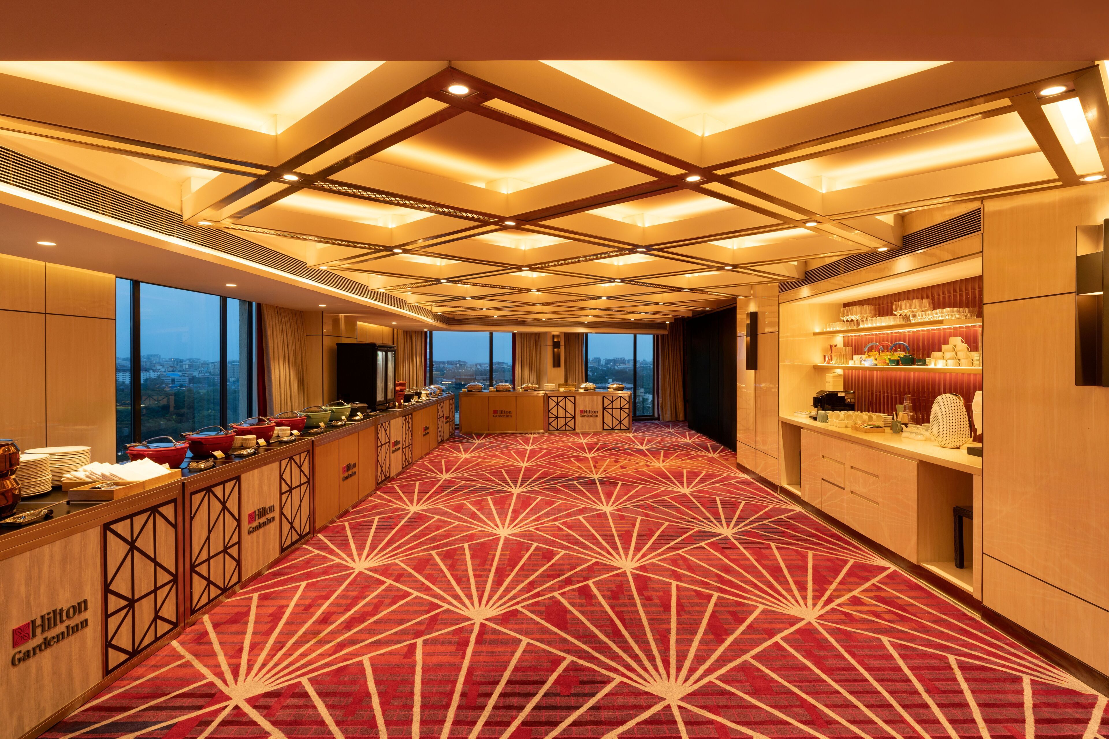 A hotel lobby with a red carpet, a buffet area, and a view of the cityscape through large windows.