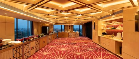 A hotel lobby with a red carpet, a buffet area, and a view of the cityscape through large windows.