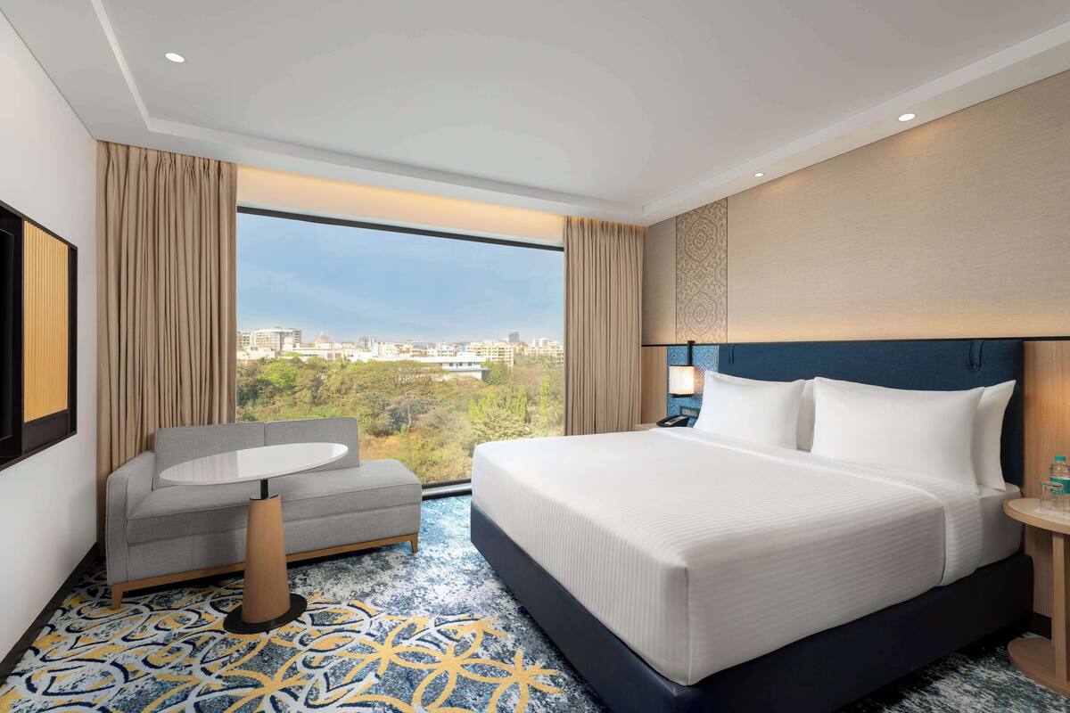 Habitación de hotel con una cama grande, un sofá, una mesita y vistas a la ciudad.