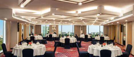 A conference room with multiple round tables, dark chairs, and a patterned carpet.