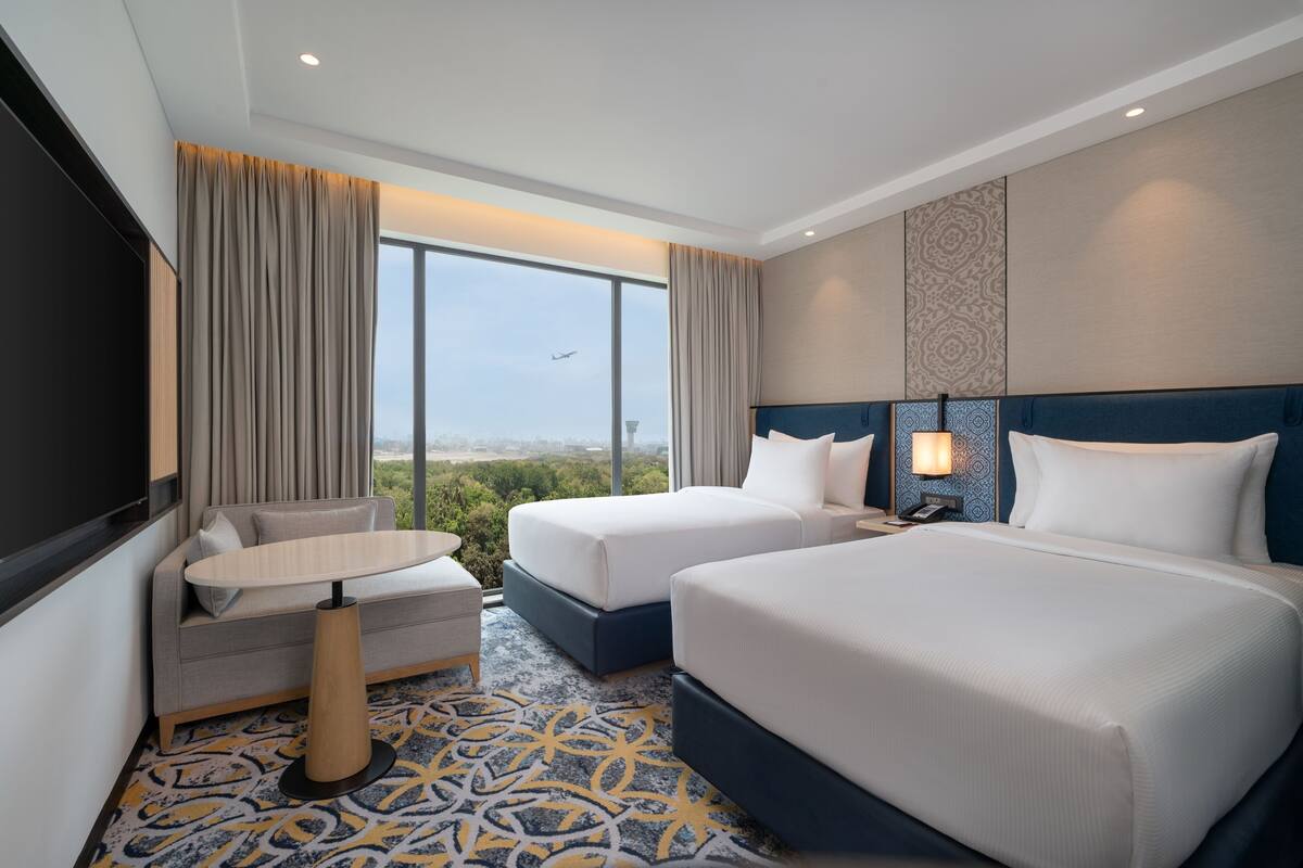 Habitación de hotel con dos camas, un sofá, una mesita y un televisor.