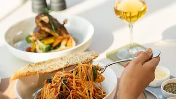 Een eettafel met een schaal spaghetti, een glas witte wijn en een bord eten.