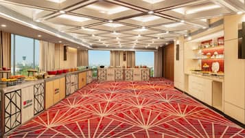 A hotel room with a red patterned carpet, a minibar, and a view of the cityscape.