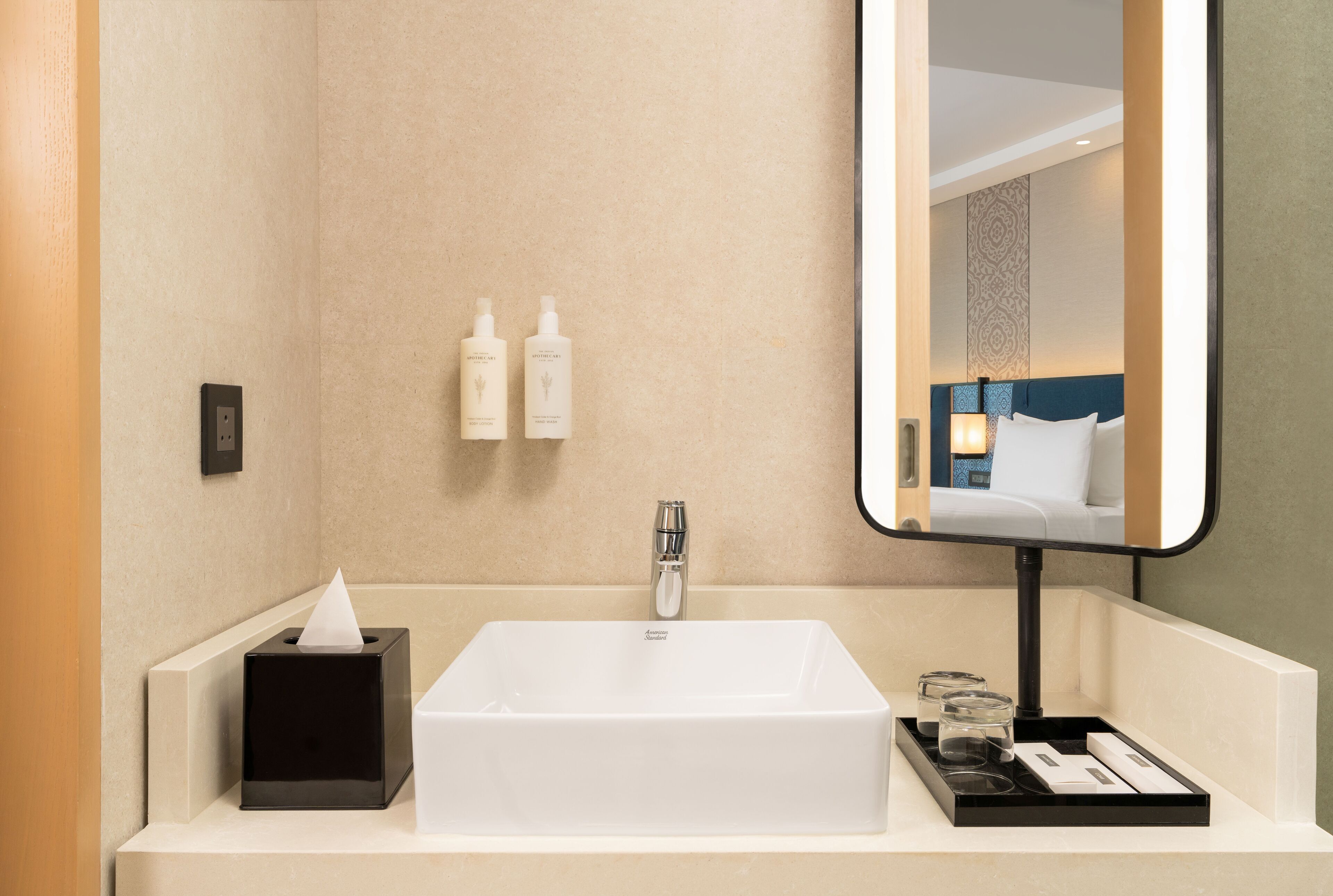 A hotel bathroom with a white sink, a mirror, and toiletries on the wall.