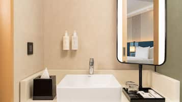 Une salle de bain d’hôtel avec un lavabo blanc, un miroir et des articles de toilette fixés au mur.
