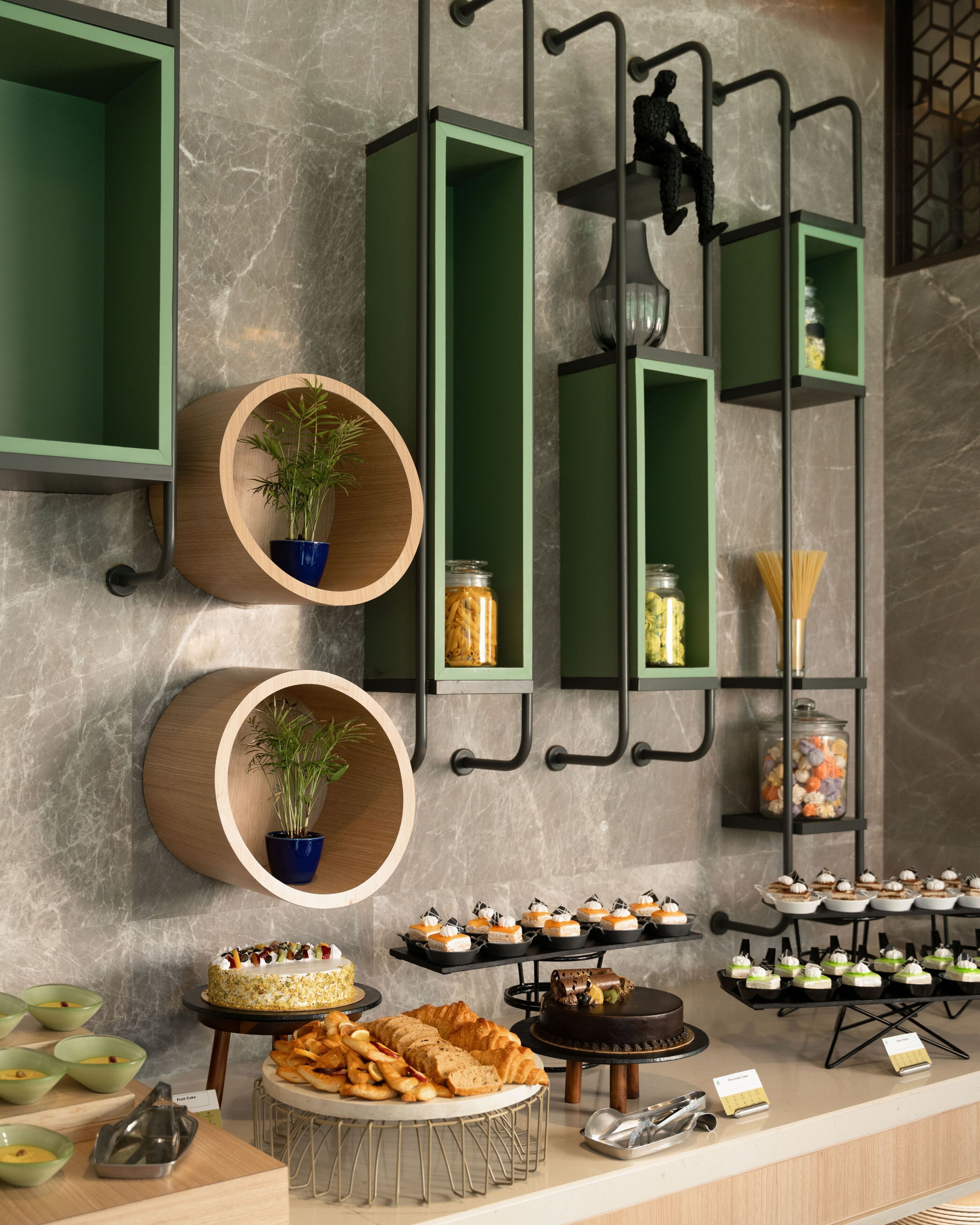 A modern kitchen with marble countertops, green cabinetry, and a variety of food items displayed.