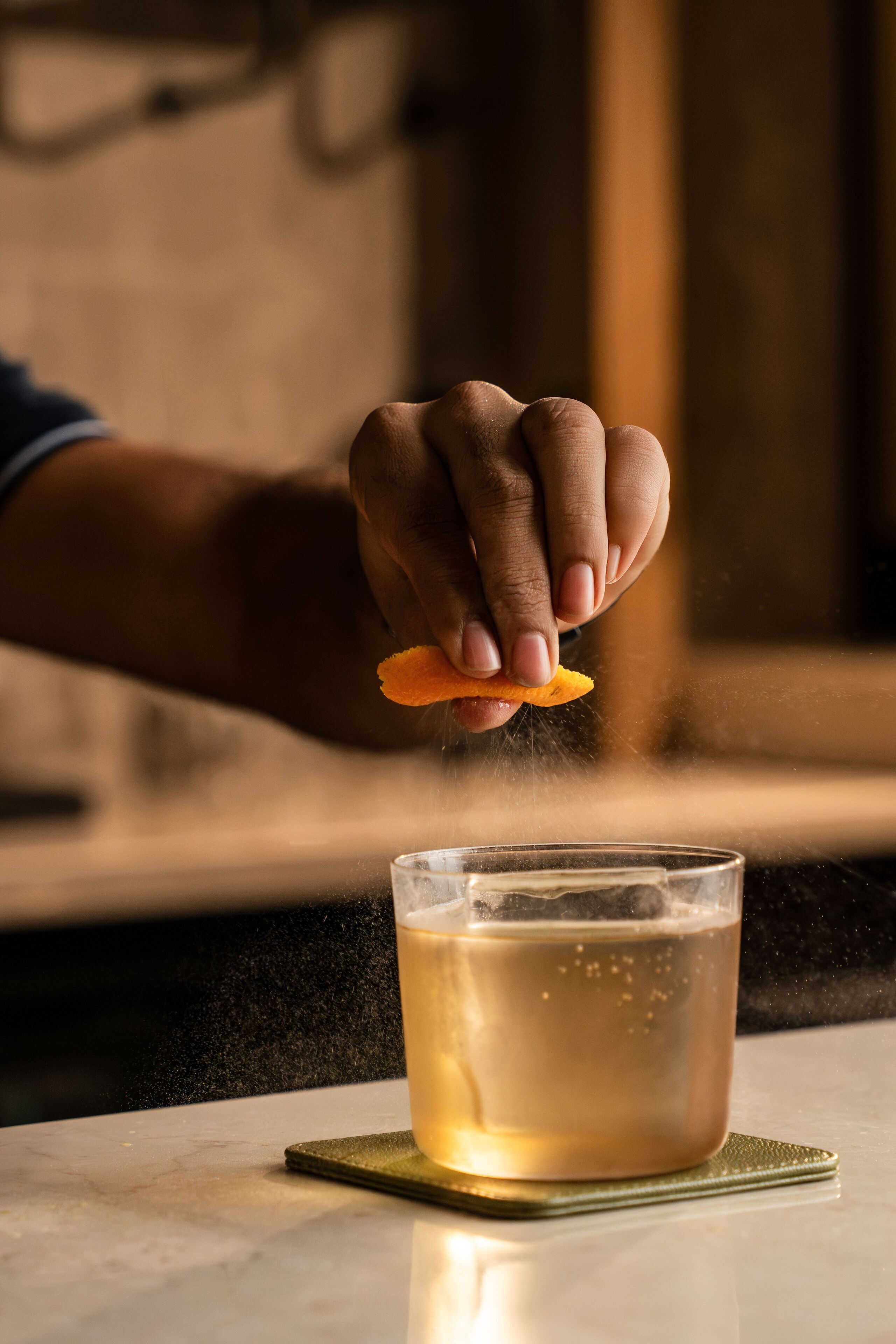 Une main saupoudre une épice dans un verre transparent contenant un liquide ambré, posé sur un comptoir en marbre.
