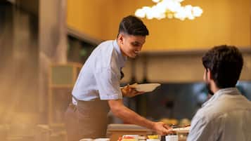 A waiter serving food to a guest in a well-lit dining area with a chandelier.