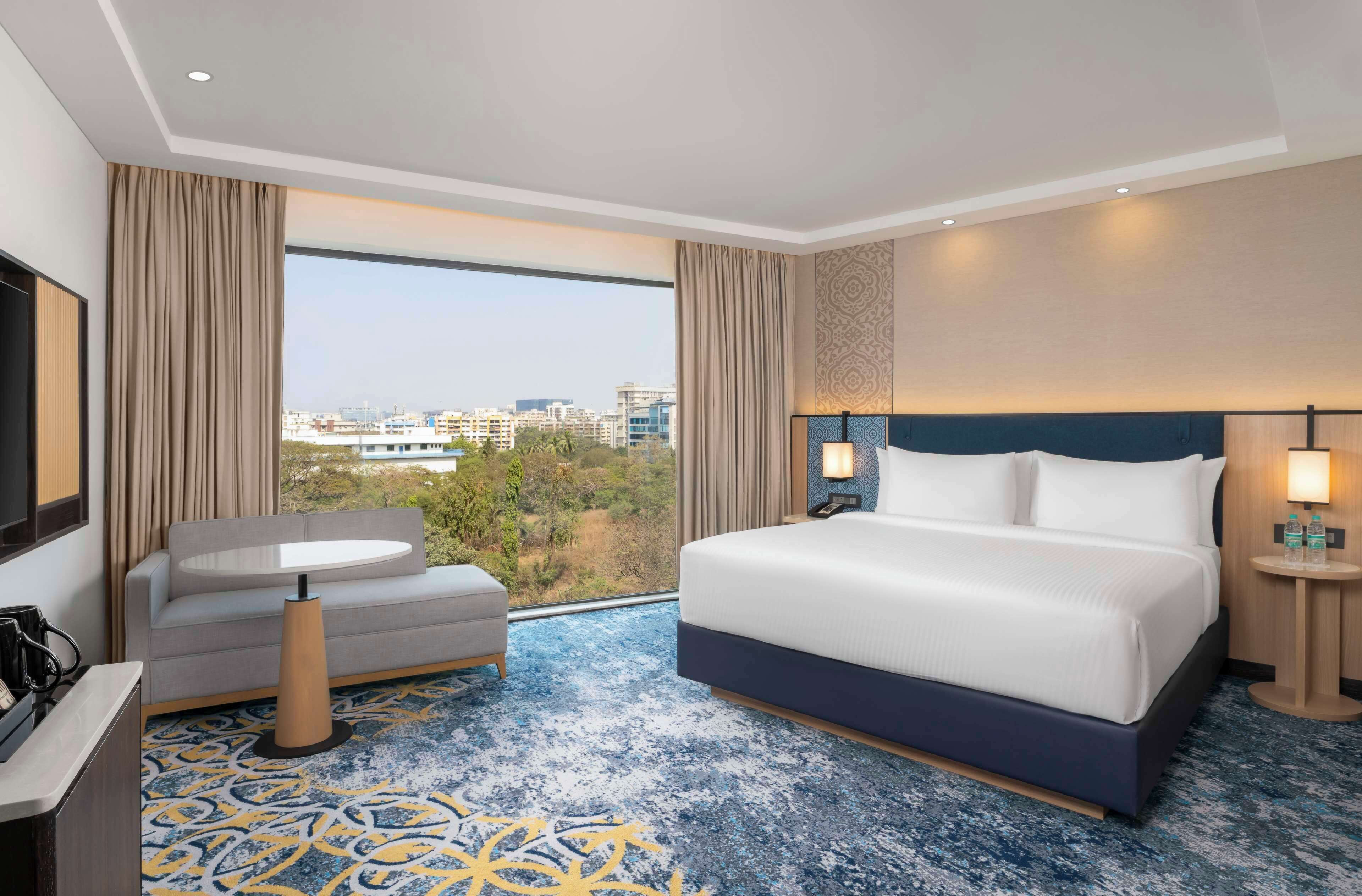 Una habitación de hotel con una cama grande, un sofá, una mesita y vistas a la ciudad.