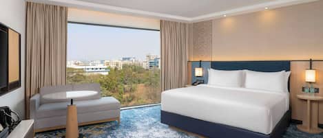Una habitación de hotel con una cama grande, un sofá, una mesita y vistas a la ciudad.