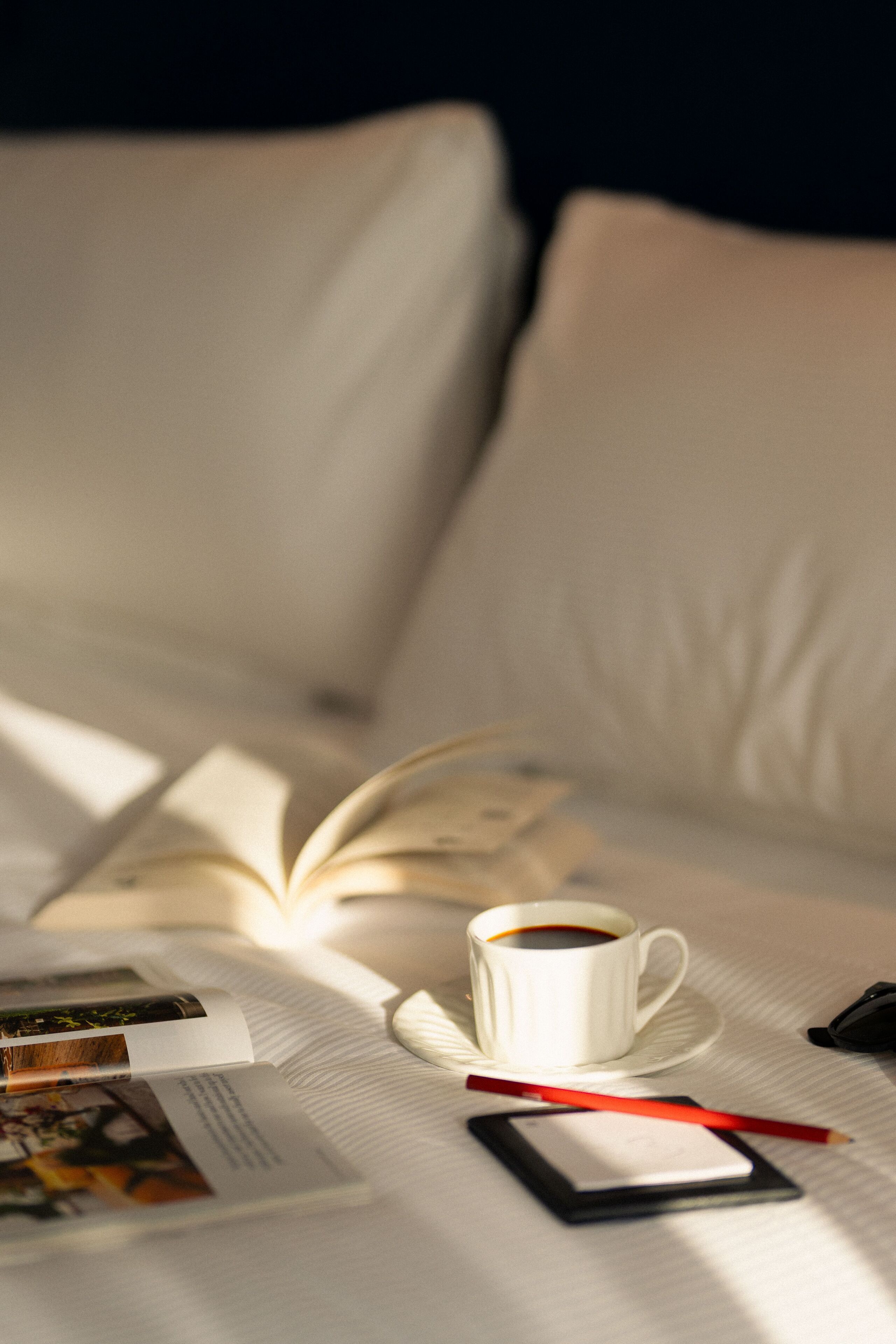 A bed with a book, a cup of coffee, and a smartphone on a white bedspread.