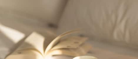 A bed with a book, a cup of coffee, and a smartphone on a white bedspread.