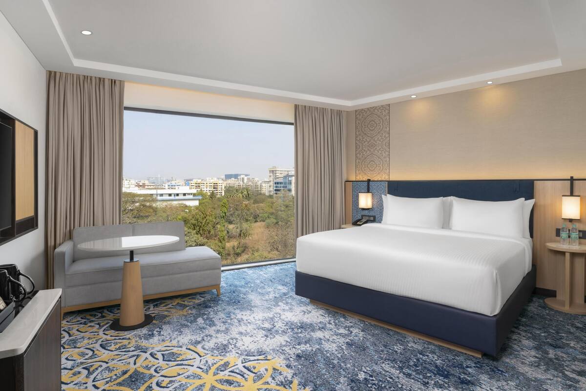 Habitación de hotel moderna con una cama grande, un sofá, una mesita y vistas a la ciudad.