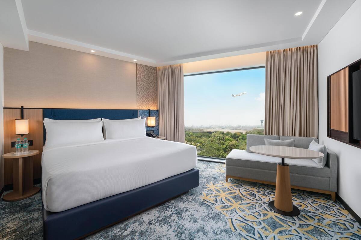 Una habitación de hotel con una cama grande, un sofá, una mesita y un televisor.