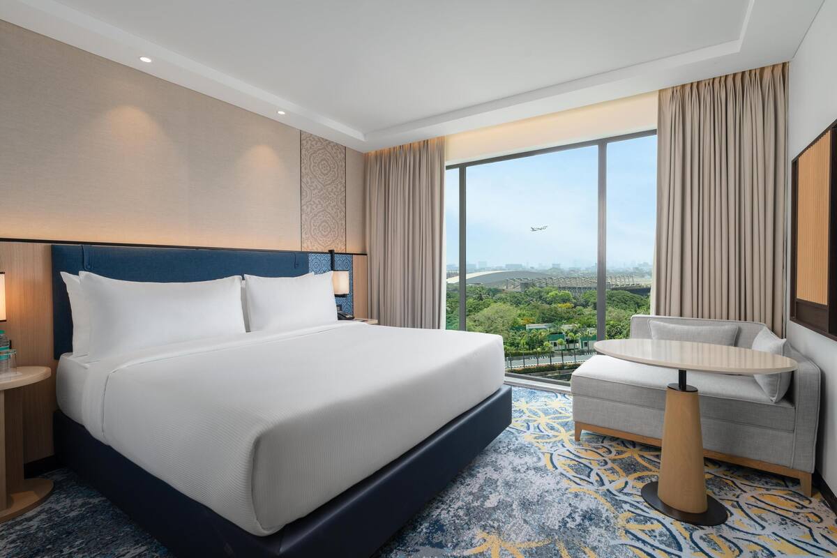 Habitación de hotel con una cama grande, un sofá, una mesita y vistas a la ciudad.