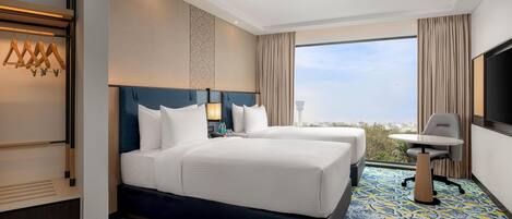 Habitación de hotel con dos camas, un escritorio y un ventanal con vistas a la ciudad.