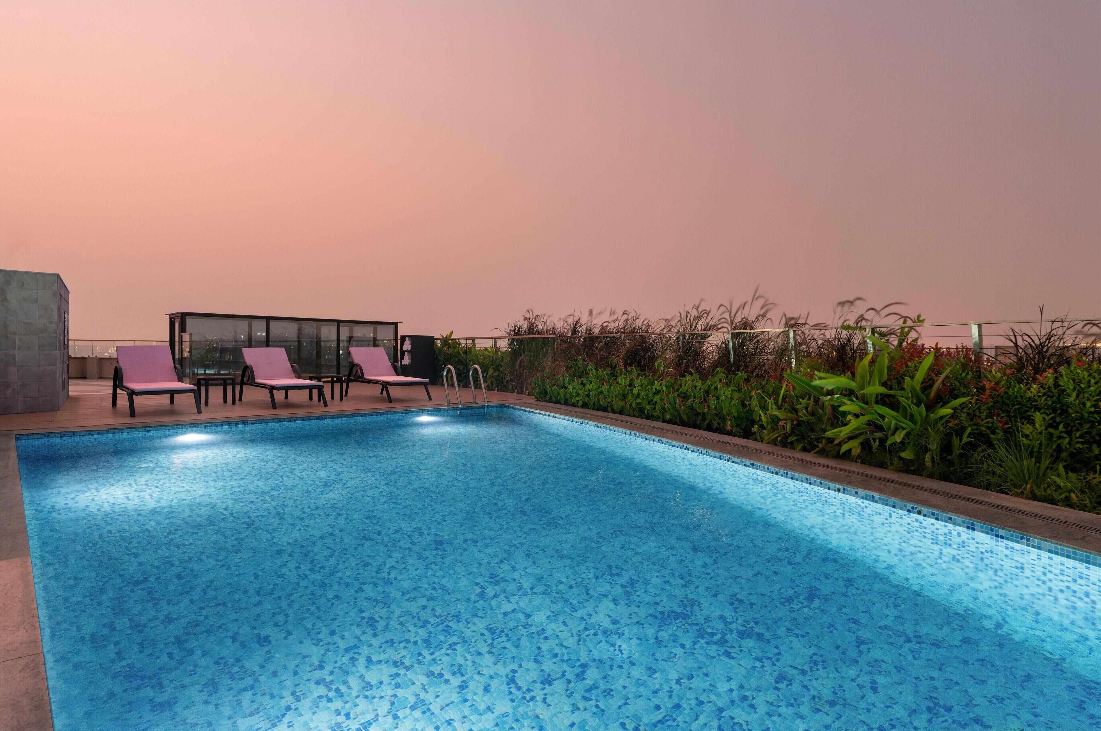 A rectangular swimming pool with a tiled edge, surrounded by lounge chairs and a small seating area with a table and chairs.