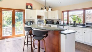 A modern kitchen with a central island, bar stools, and a large window offering a view of the outdoors. - Beaufiul Sonoma house on large property in vineyards with lots of amenities! (Sonoma)