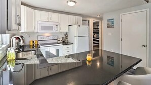 A modern kitchen with white cabinets, a black countertop, a microwave, a refrigerator, and a sink.