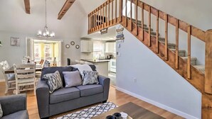 A modern living room with a grey sofa, wooden staircase, and a view into the kitchen.