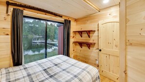 A wooden cabin room with a bed, a sliding glass door to a dock, and a wooden door with shelves. - Waterfront 'Little Red Camp' on Moose River (Rockwood)