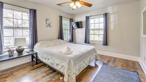 Quarto com cama, ventoinha no teto, televisão e janela com cortinas.